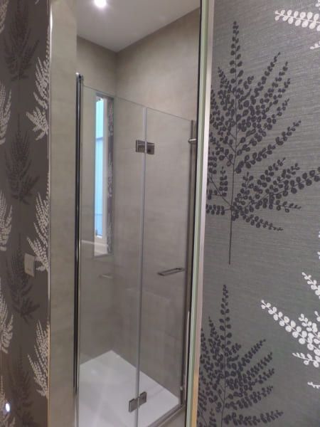 Un baño con ducha a ras de suelo y un papel pintado de helechos en la pared.