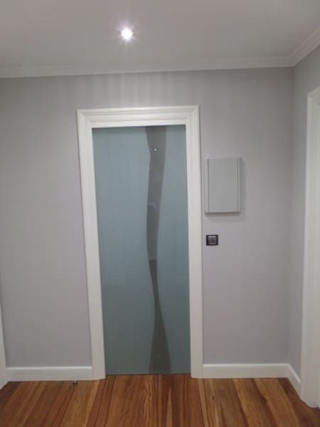 Un pasillo con puerta de cristal y suelo de madera.