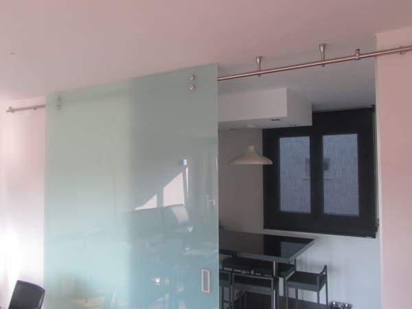 Una puerta corrediza de vidrio separa una sala de estar de una cocina.