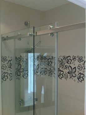 Una cabina de ducha con puertas corredizas de vidrio y un diseño floral en la pared.