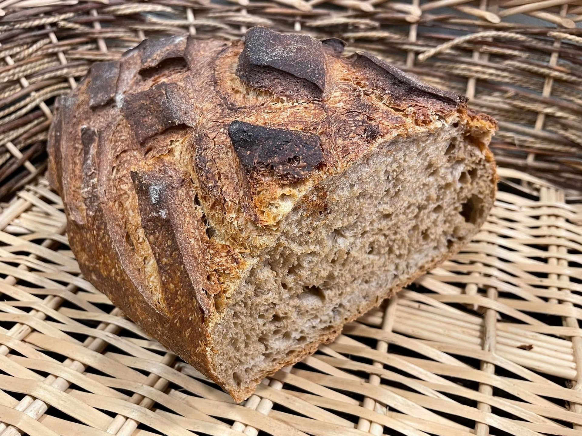 Pain rustique rond tranché artisanal à croûte foncée, présenté dans un panier en osier
