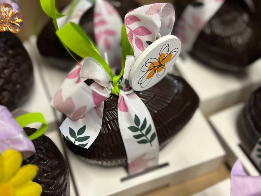 Des coupes de dessert au chocolat décorées de rubans blancs à motifs et de feuilles vertes, présentées sur un plateau.