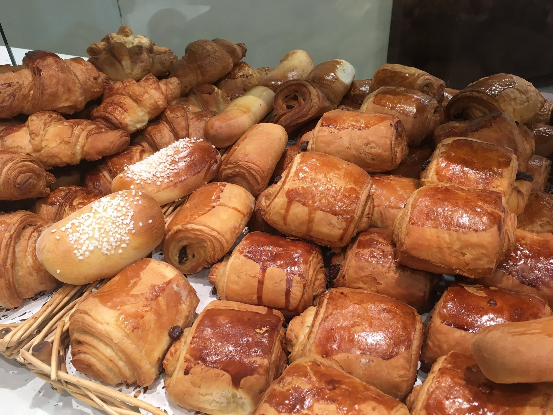 Assortiment de viennoiseries et de croissants dorés, présentés dans une vitrine de boulangerie.