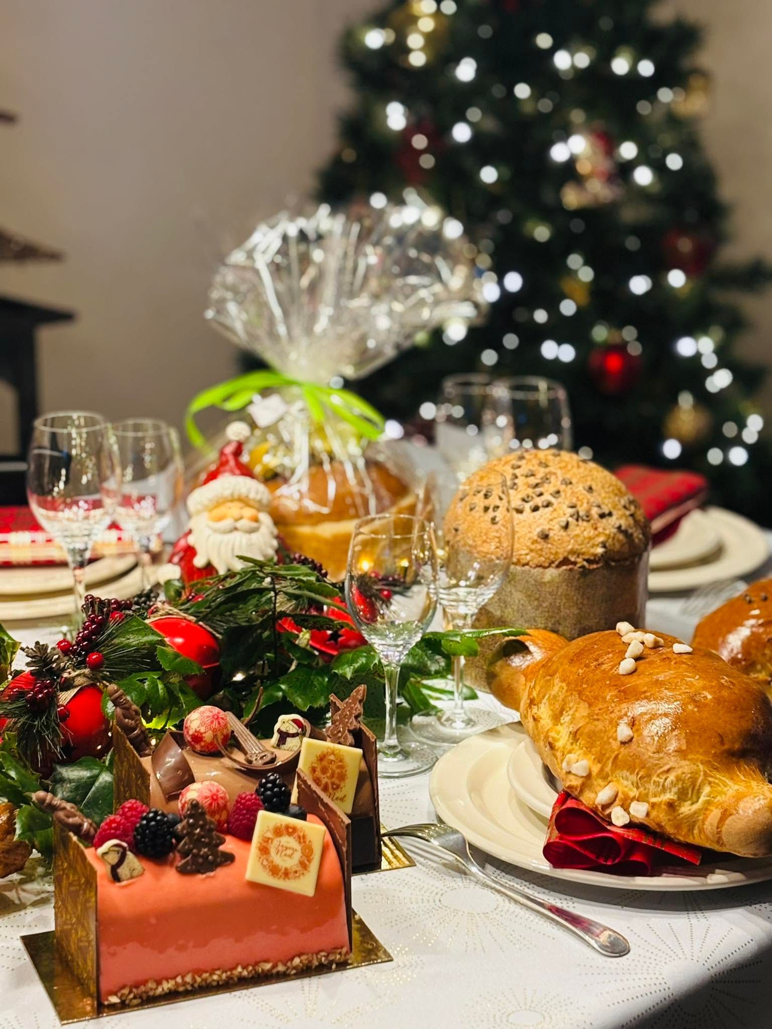 Table de fête avec plateaux de desserts, pain, vin et un sapin de Noël en arrière-plan.