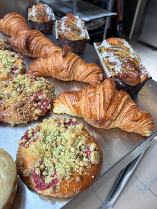 Assortiment de viennoiseries sur un plateau, comprenant des croissants et des tartelettes à crumble, dans une vitrine de boulangerie.