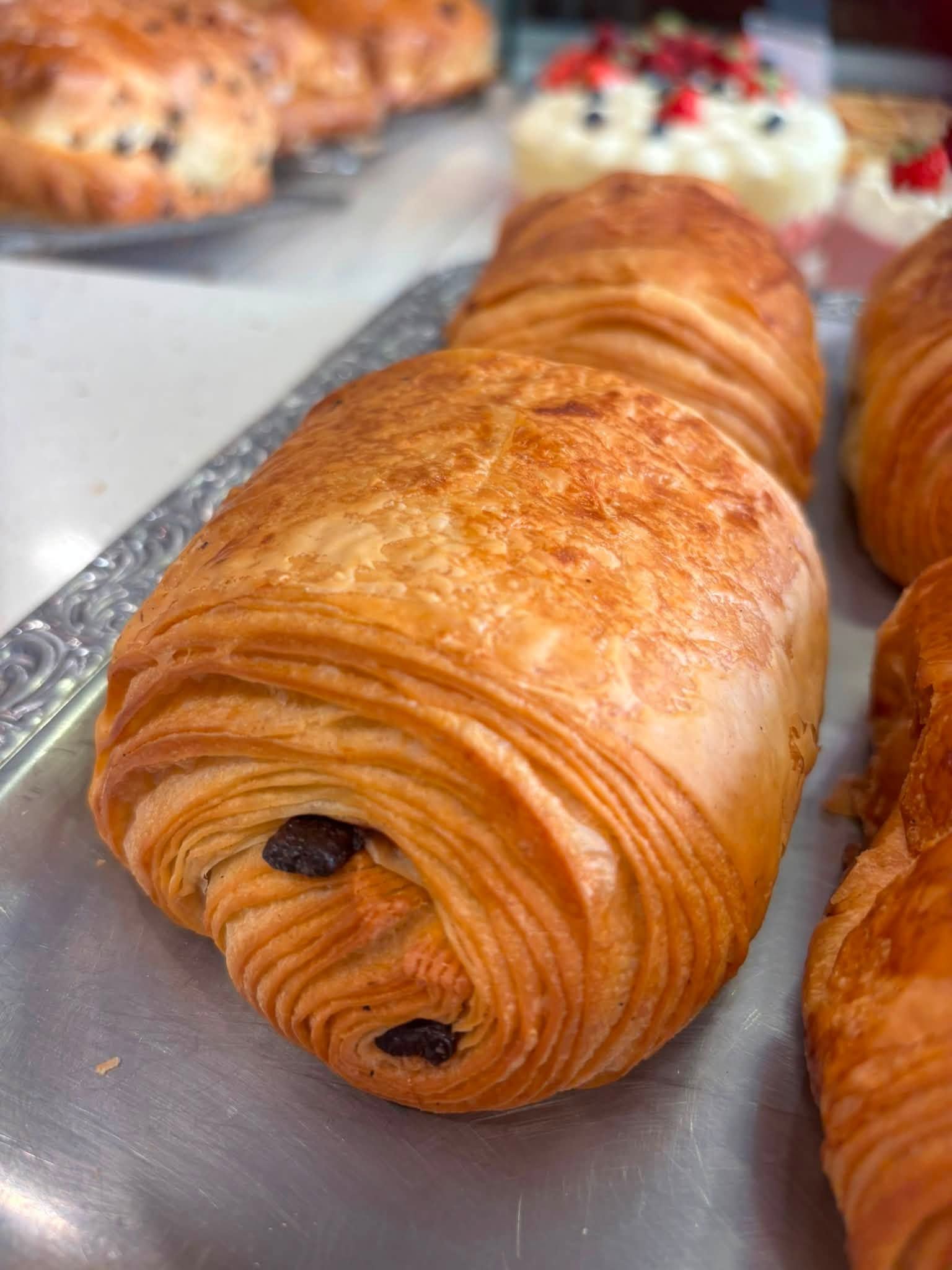 Pain au chocolat doré sur un plateau, avec d'autres pâtisseries floues en arrière-plan.
