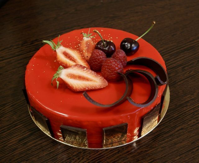 Gâteau recouvert d'un glaçage rouge décoré de fraises, de framboises, de cerises et de copeaux de chocolat.