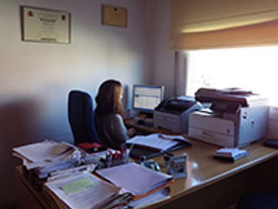 Una mujer está sentada en un escritorio frente a una computadora y una impresora.