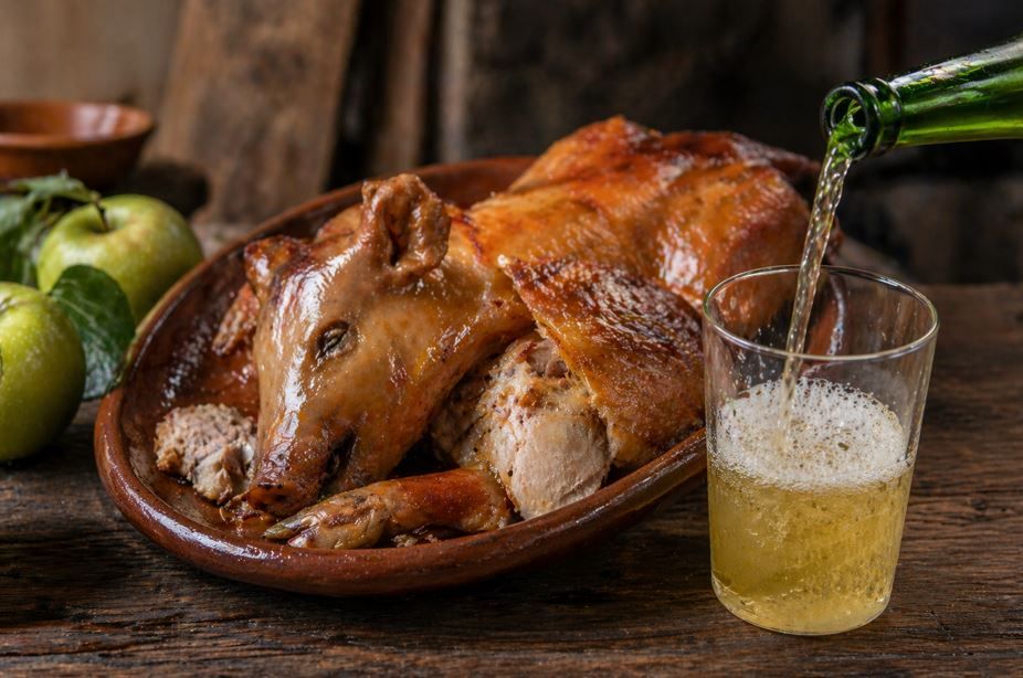 Cerdo entero asado en una fuente con un vaso de cerveza sobre una mesa rústica de madera.