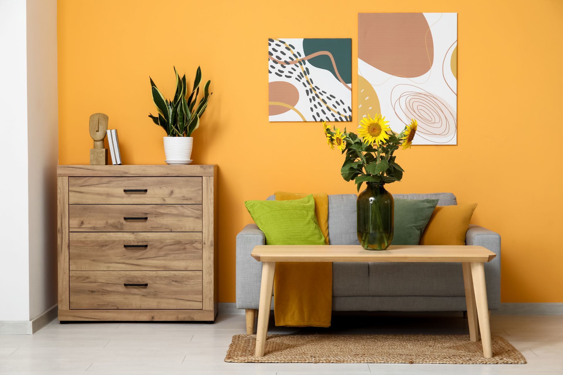 Salon avec des murs jaunes, un canapé gris, une table et une commode en bois.