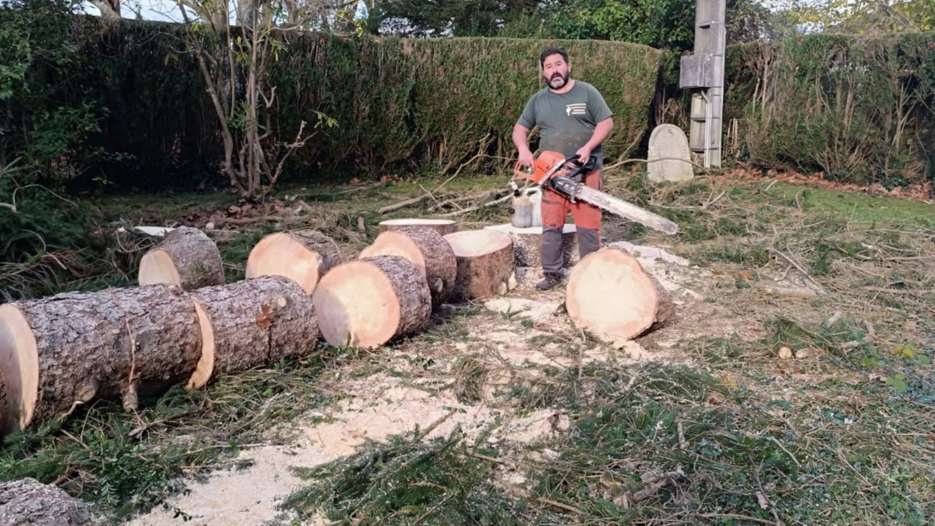 Un homme coupe un tronc à la tronçonneuse dans une cour.