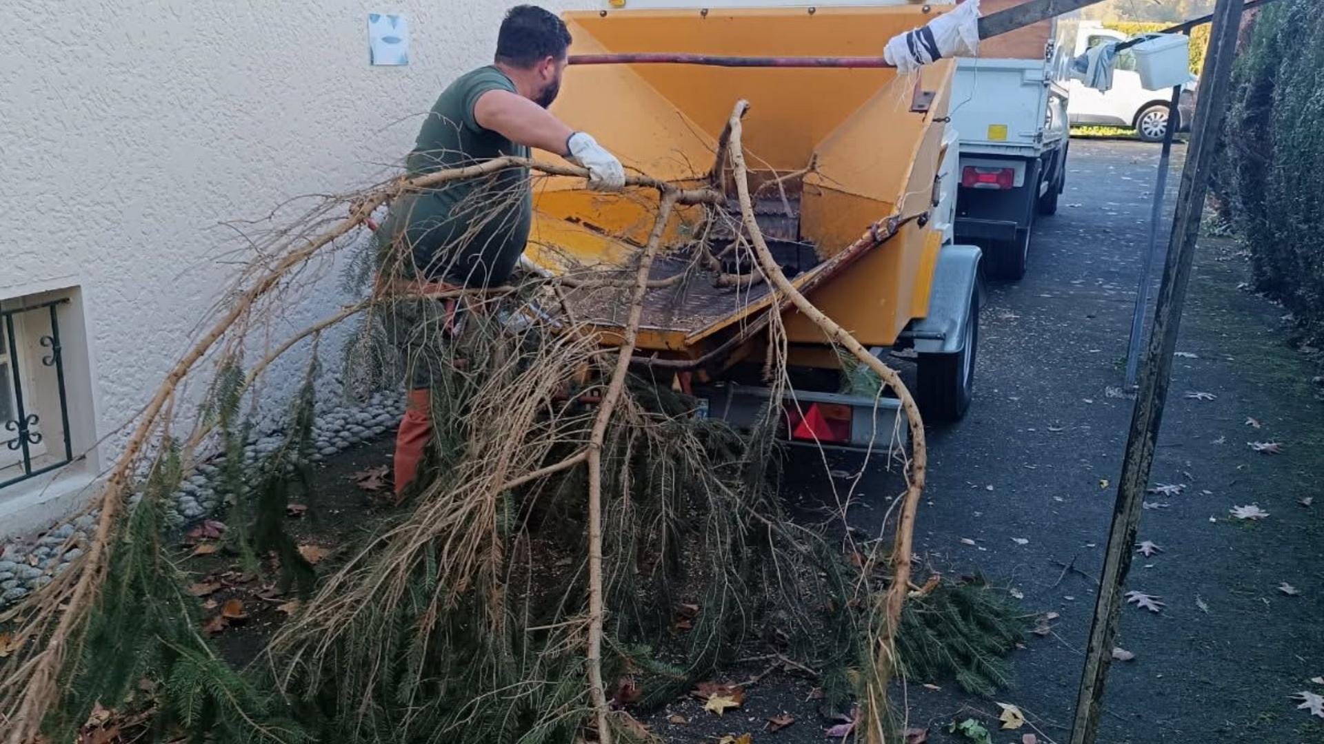 Une personne alimente un broyeur de branches jaune monté sur une remorque.