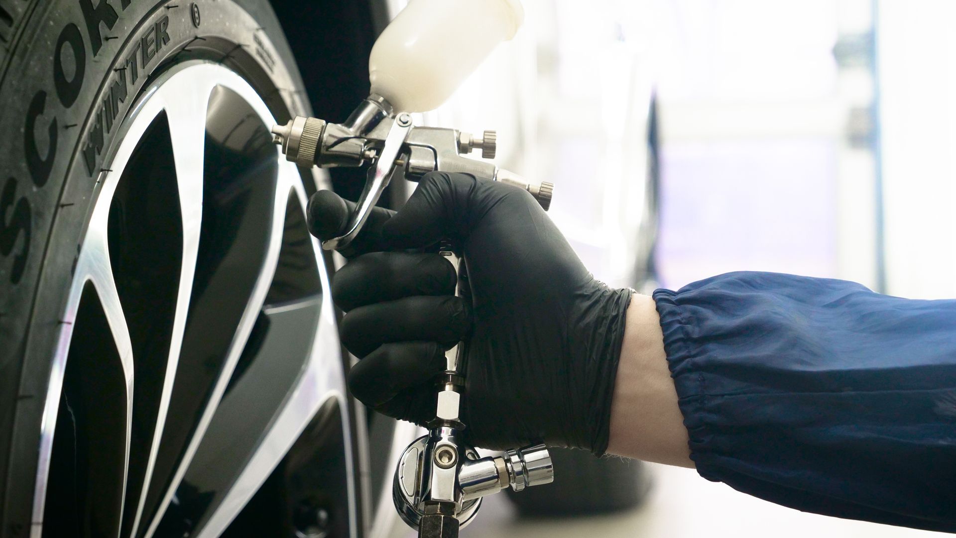 Une personne portant un gant noir peint une jante de voiture à la bombe avec un pistolet à peinture.