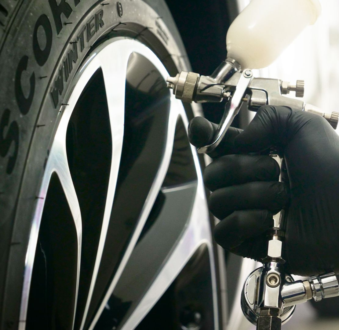 Une main gantée vaporise de la peinture sur une jante de voiture. La jante est noire et argentée.