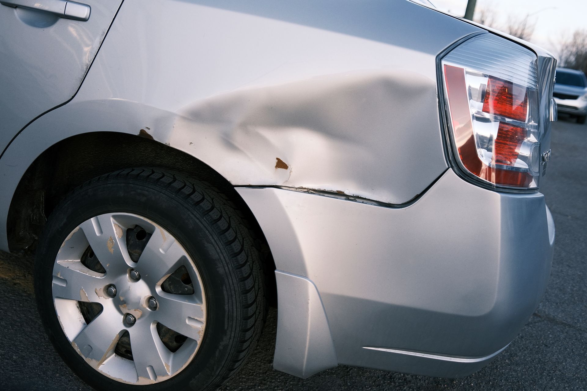Voiture argentée avec un important enfoncement sur l'aile arrière.