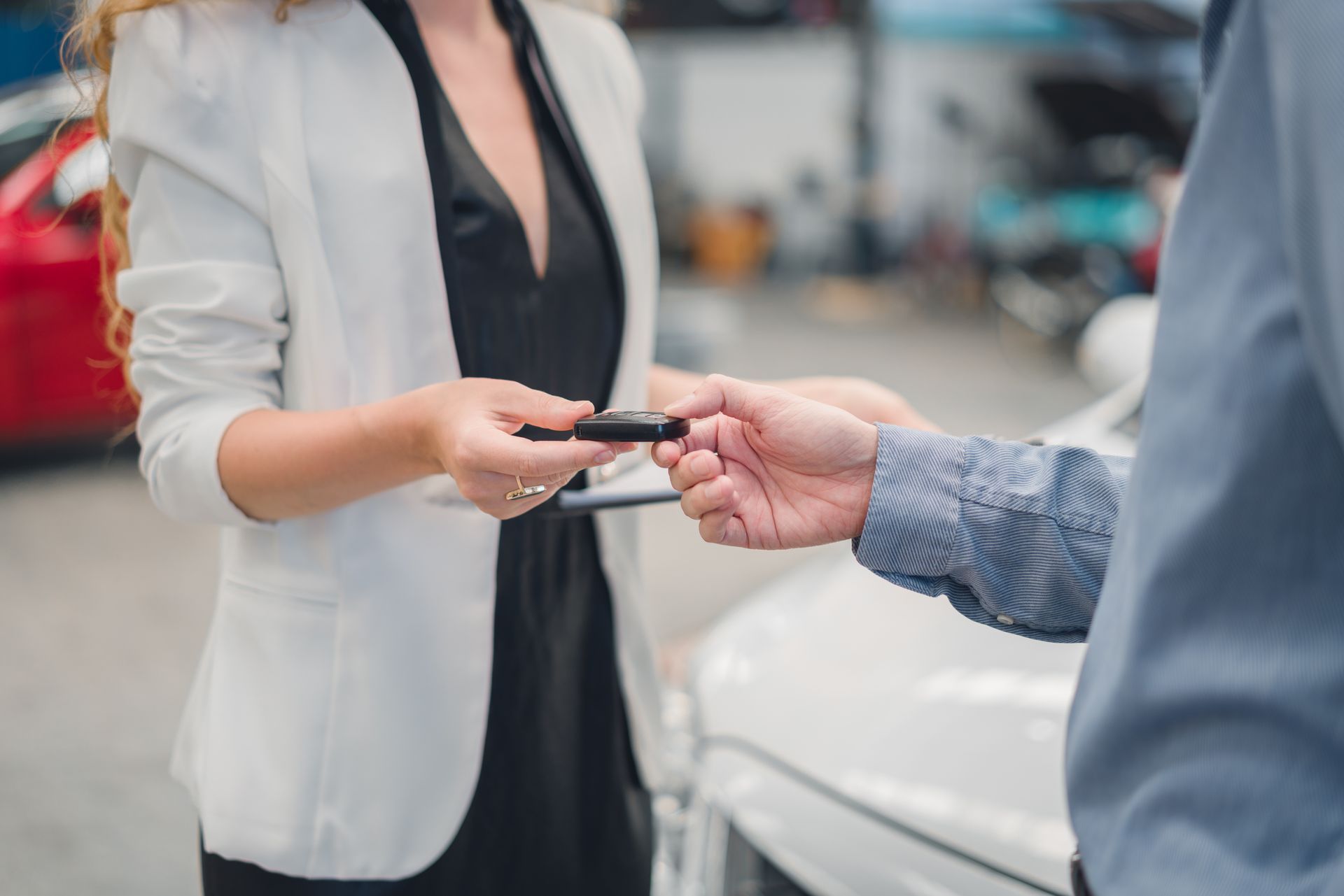 Une femme en blazer tend des clés de voiture à une personne en chemise bleue, à côté d'une voiture blanche.