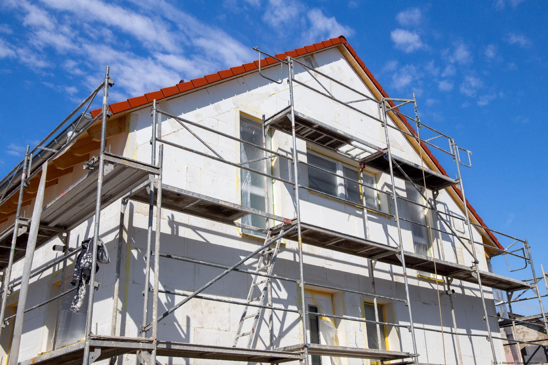 Hausfassade mit Gerüst bei Sanierung eines Einfamilienhauses unter blauem Himmel