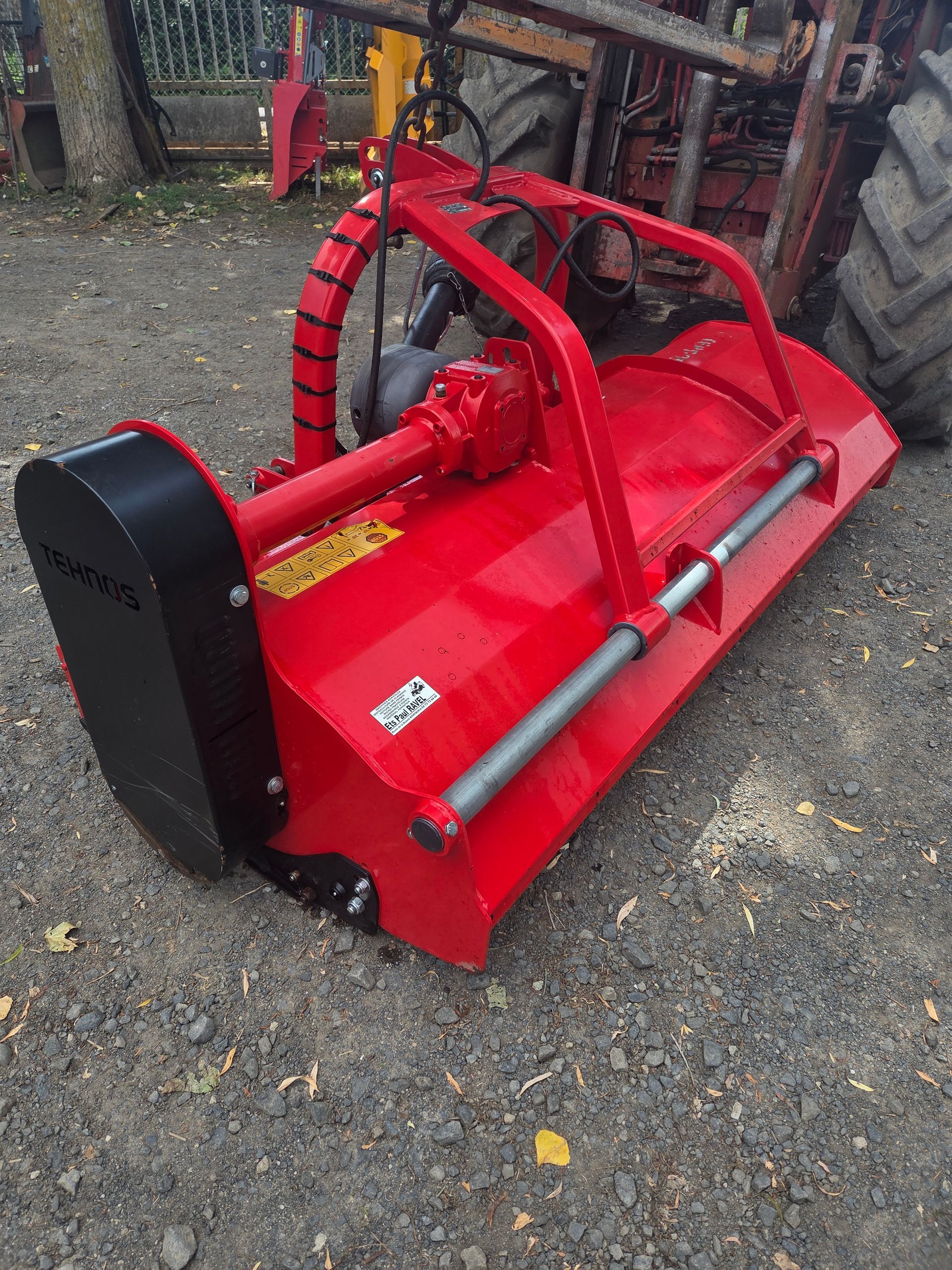 Accessoire de tracteur rouge sur du gravier, marqué « VENDU » en grandes lettres turquoise.