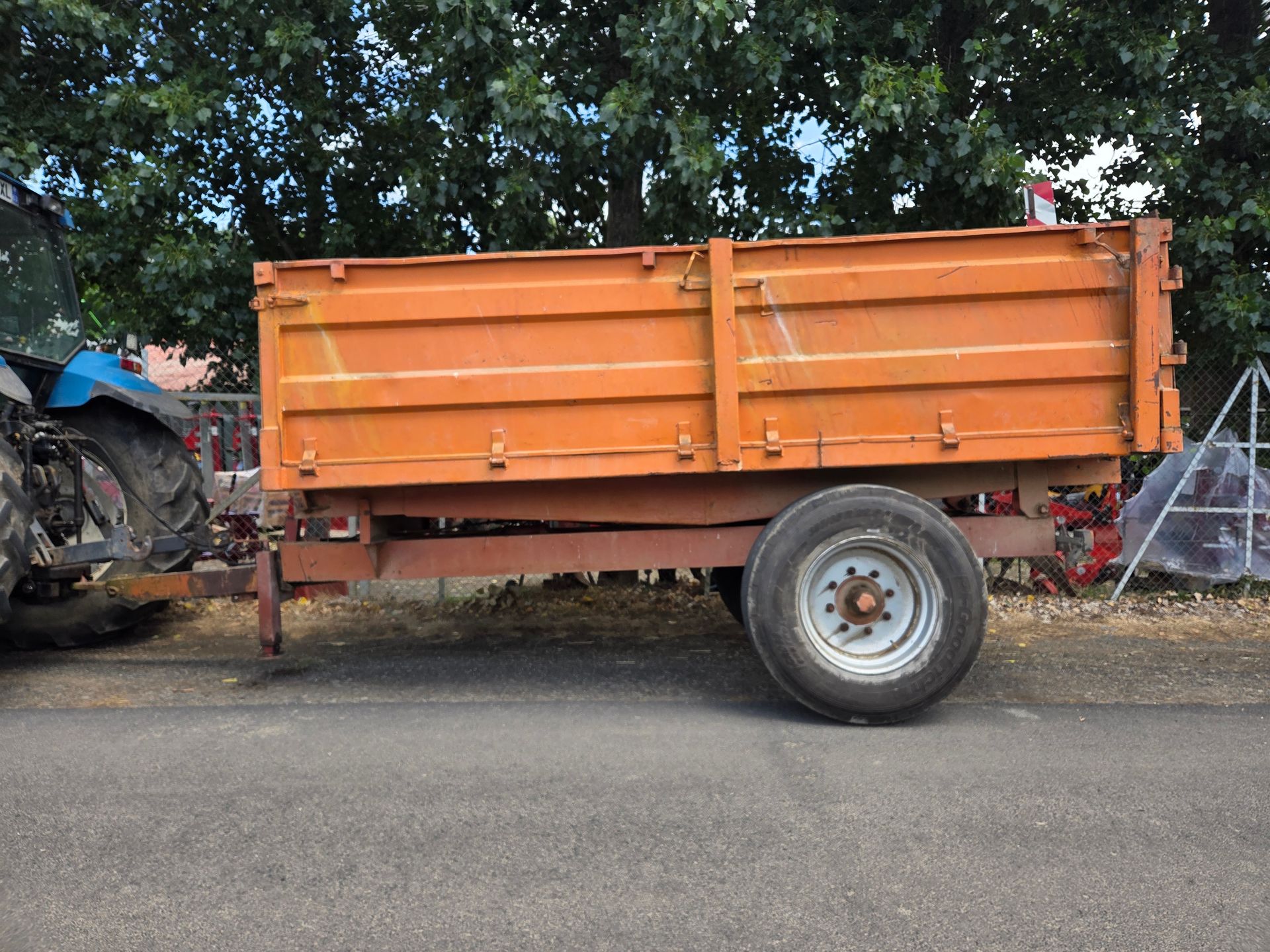 Une remorque agricole rouge avec une grande pancarte rouge « VENDU » garée dans une rue ensoleillée.