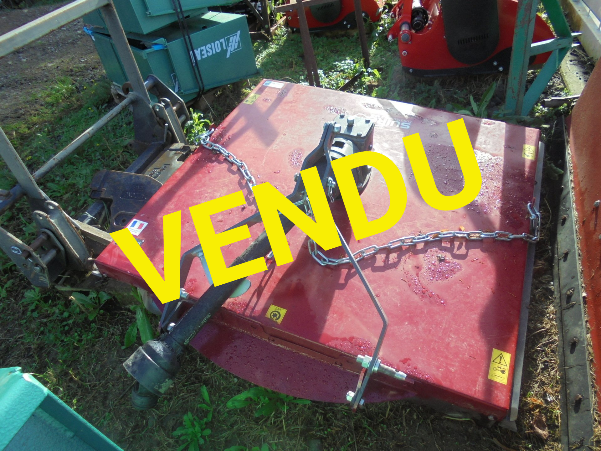 Panneau de machines rouges avec une grande enseigne jaune « VENDU » dans une cour extérieure.