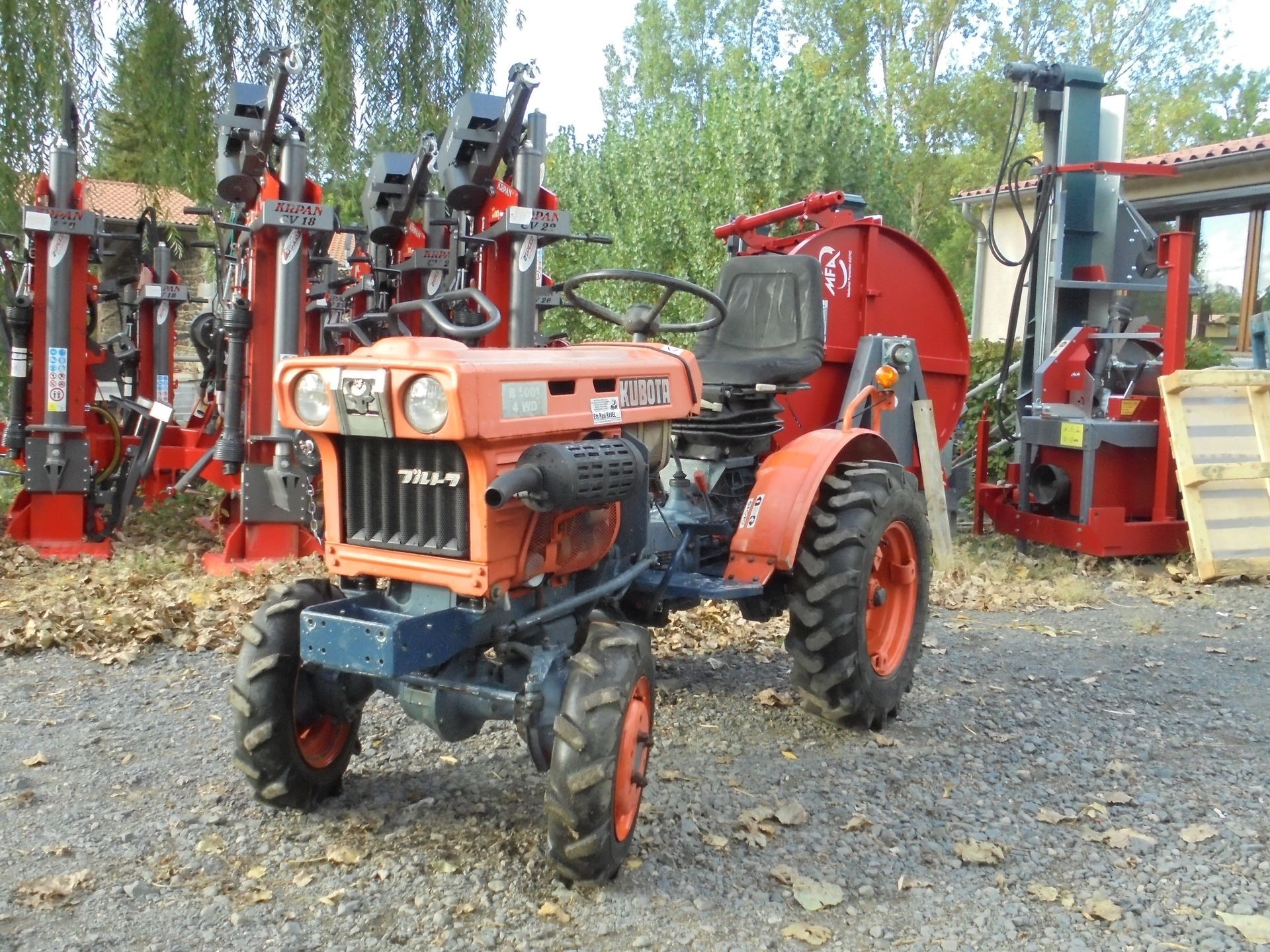 Un tracteur orange est garé devant un magasin de matériel agricole vert, d'autres tracteurs se trouvant à proximité.