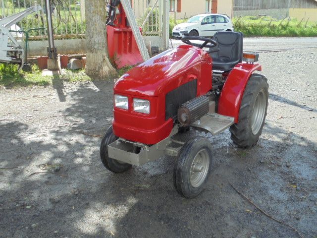 Tracteur rouge stationné sur un chemin de terre à côté d'un autre tracteur, vu de l'avant gauche