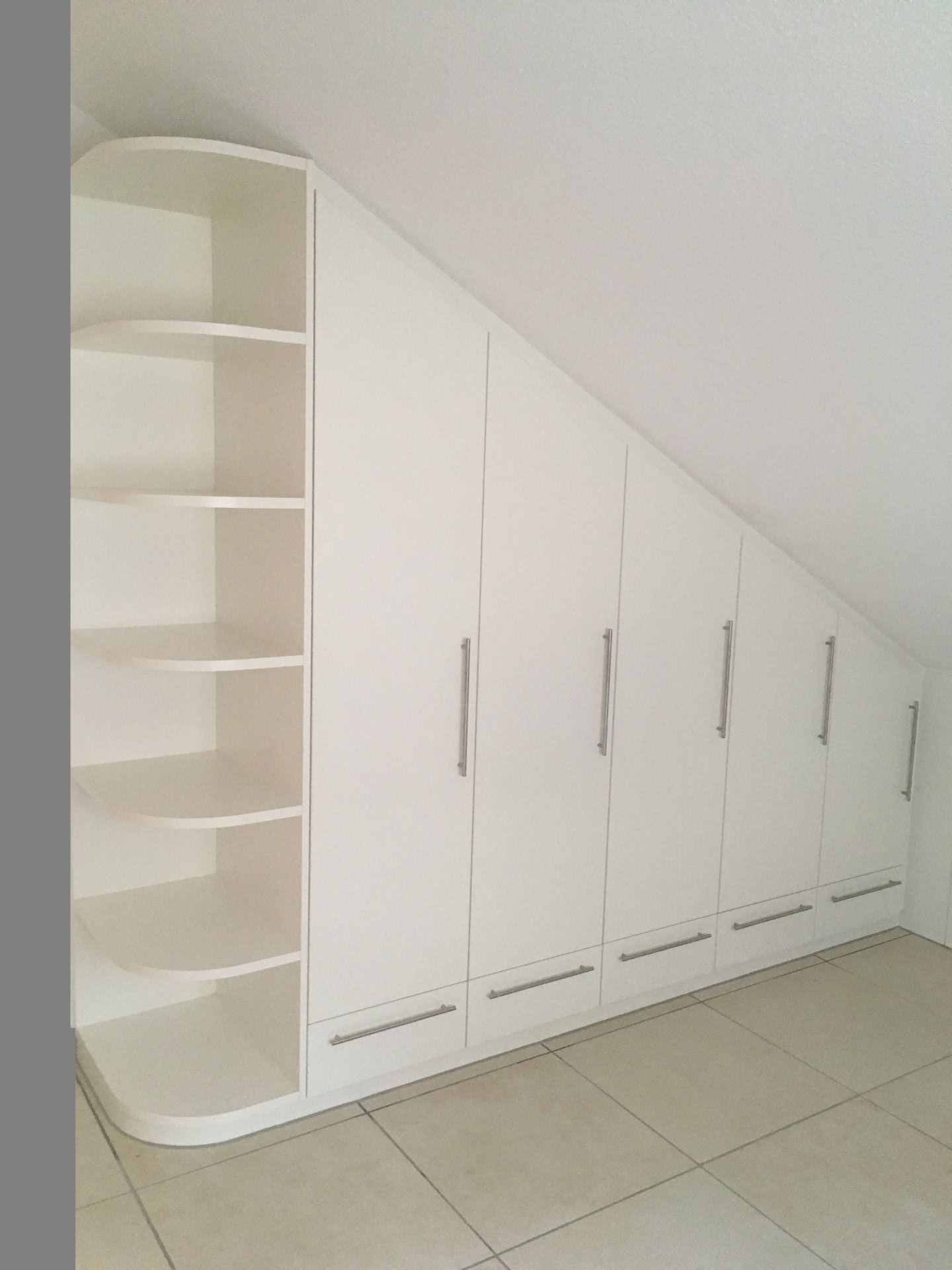 Ein weißer Schrank mit Schubladen und Regalen unter einer Dachschräge.