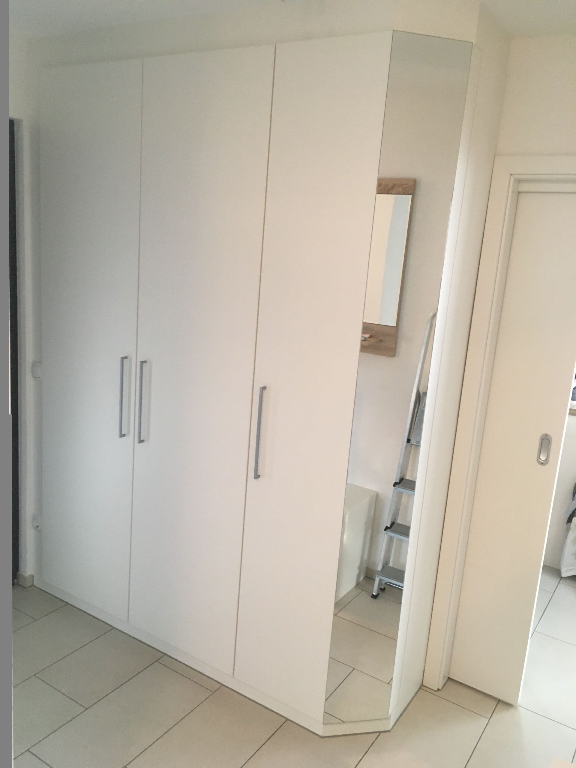 Ein weißer Kleiderschrank mit Spiegel und Leiter in einem Flur.