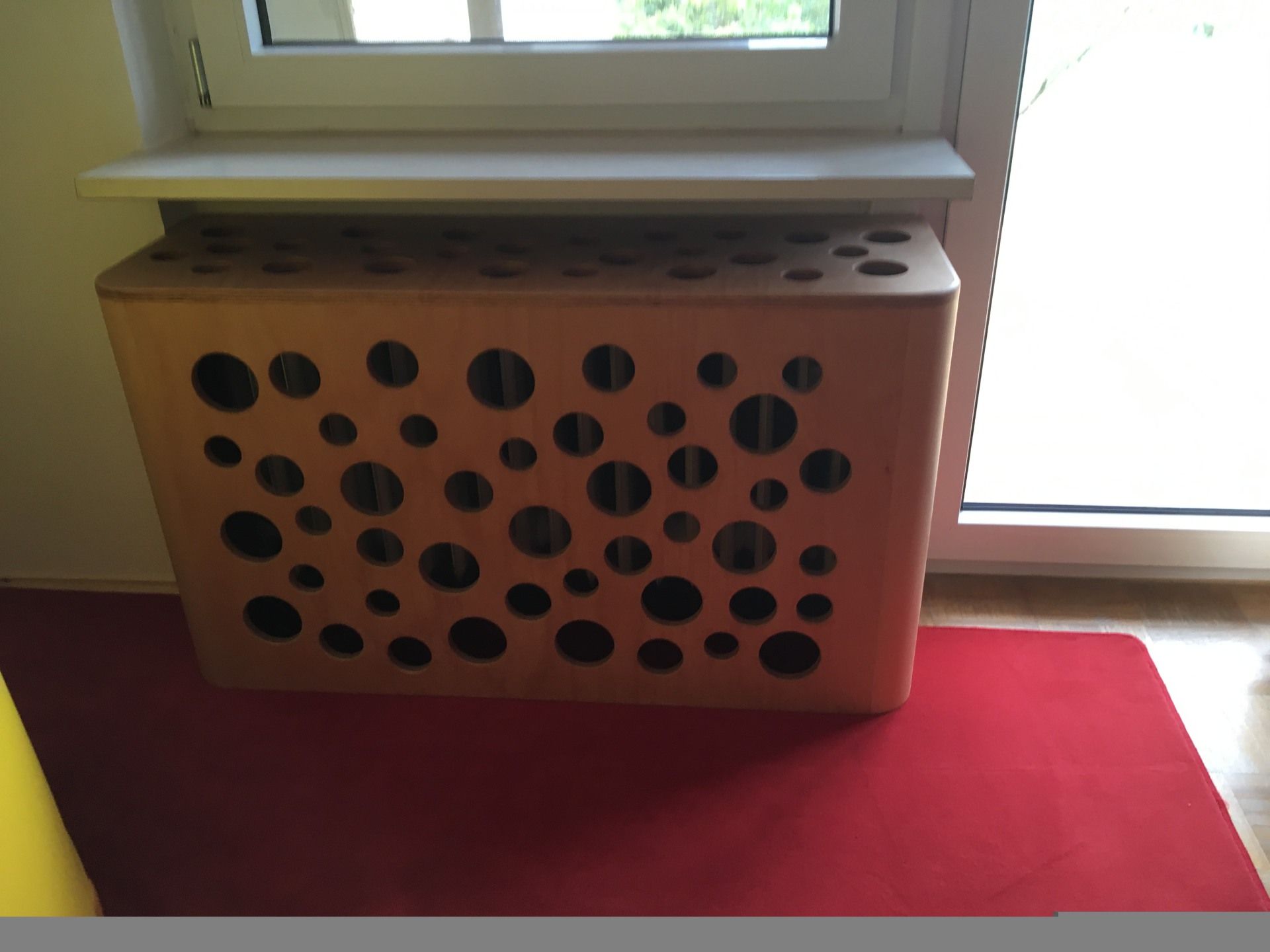 Neben einem Fenster steht eine Holzkiste mit Löchern.