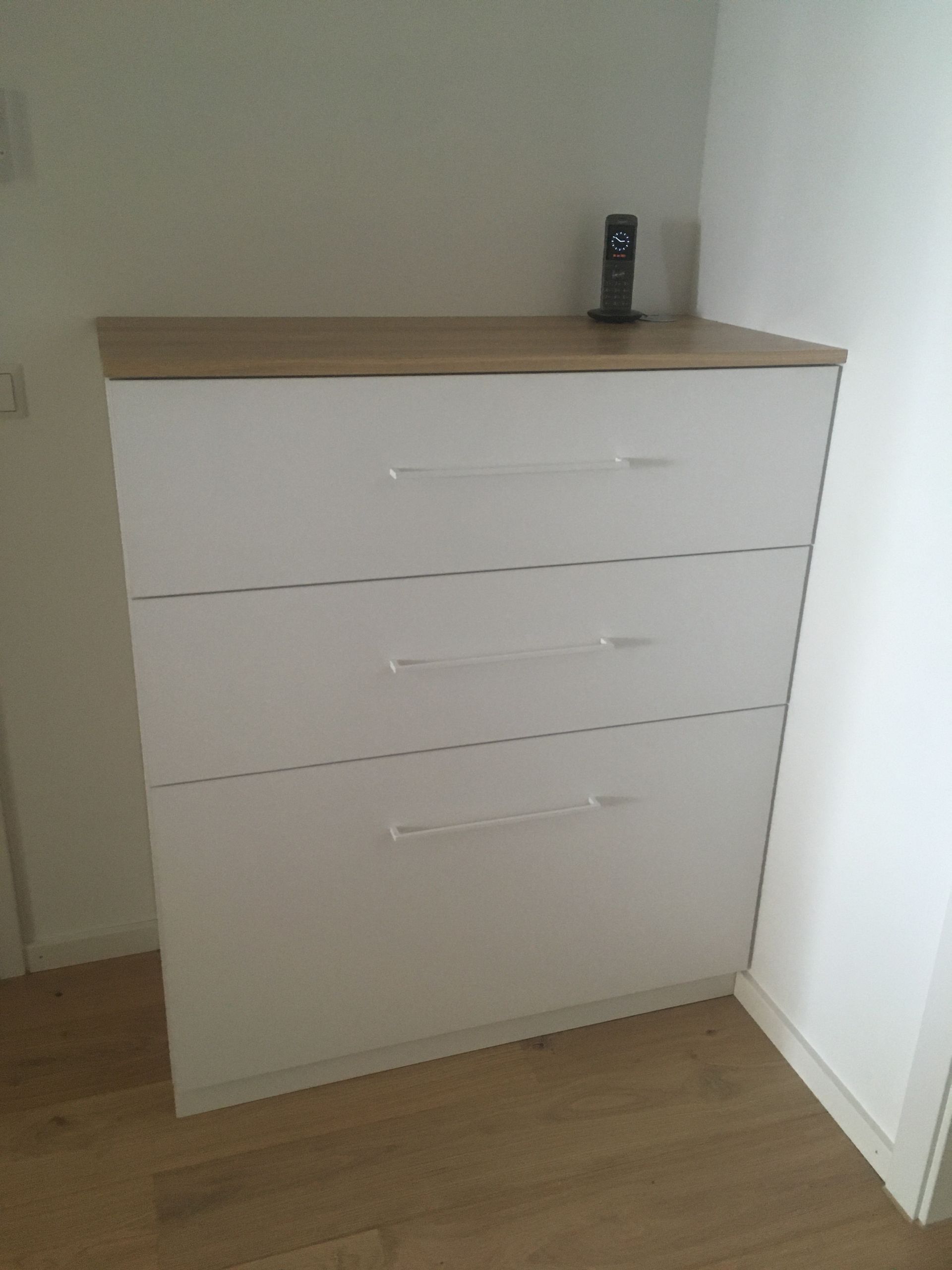 Eine weiße Kommode mit drei Schubladen und einem Telefon darauf.