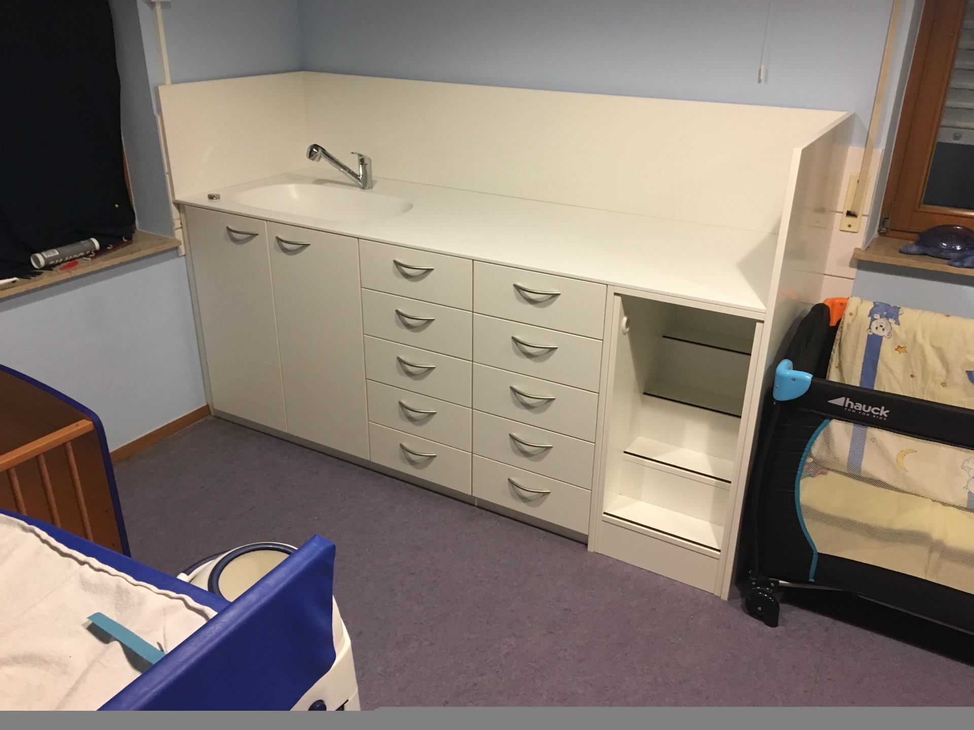 Ein Zimmer mit einem Kinderbett und einem Waschbecken.