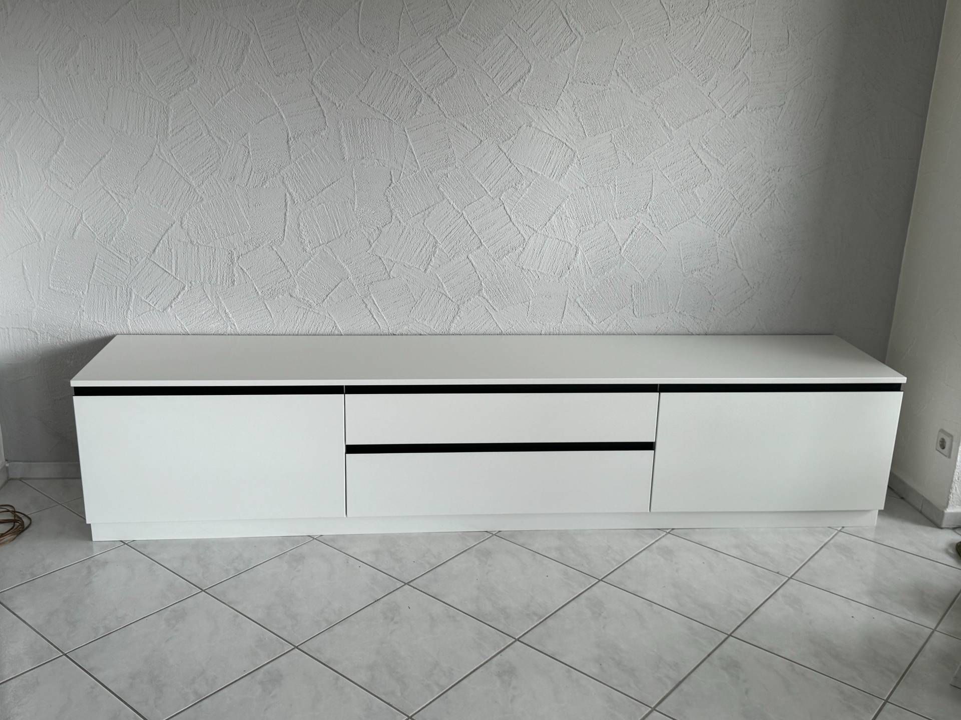 Ein weißes Entertainment-Center steht auf einem gefliesten Boden in einem Wohnzimmer.