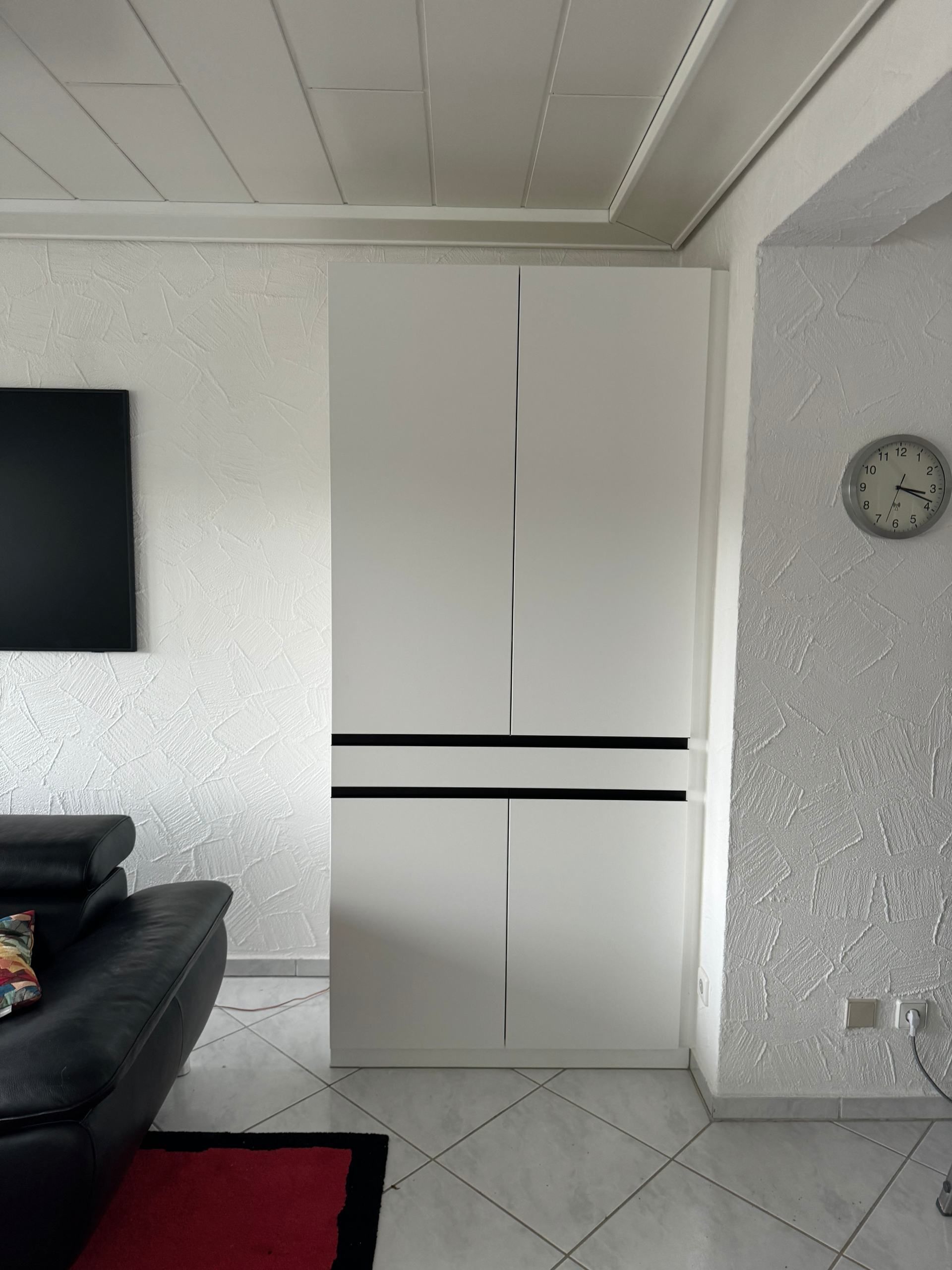 Ein Wohnzimmer mit einem schwarzen Sofa und einer Uhr an der Wand.