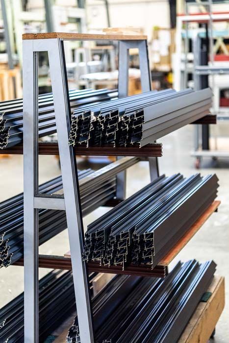 Barres métalliques empilées sur une étagère à plusieurs niveaux dans un environnement industriel.