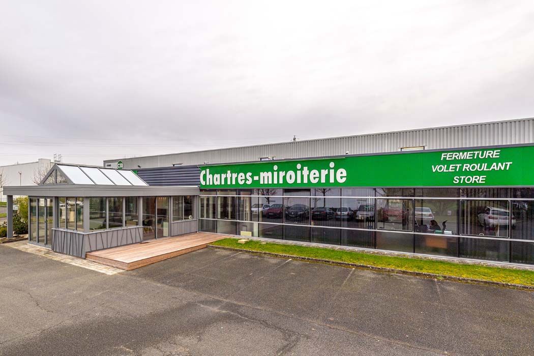Bâtiment de la Miroiterie à Chartres avec une enseigne verte par temps nuageux.