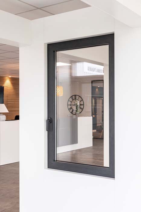 Fenêtre à cadre sombre sur un mur blanc. La fenêtre laisse entrevoir un intérieur avec une horloge et d'autres éléments décoratifs.