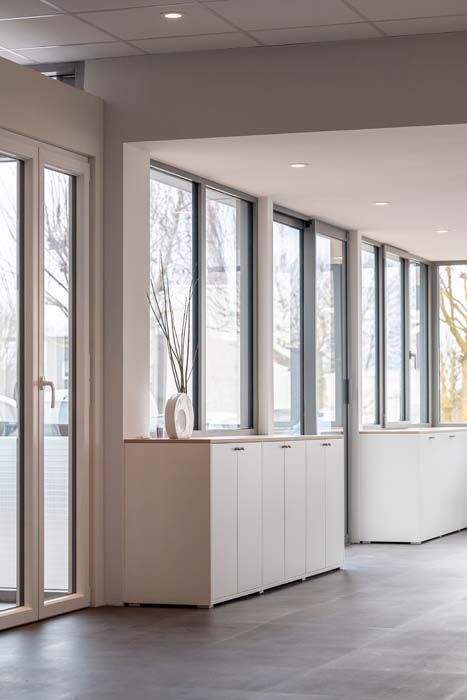 Bâtiment moderne avec de grandes baies vitrées reflétant des arbres et une pelouse verdoyante.