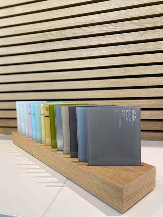 Présentoir en bois contenant une rangée d'échantillons carrés translucides colorés sur un fond en bois à lattes.