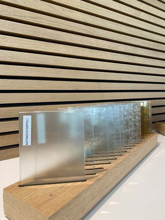 Échantillons de verre texturé dans un support en bois, contre un mur de lattes de bois horizontales.