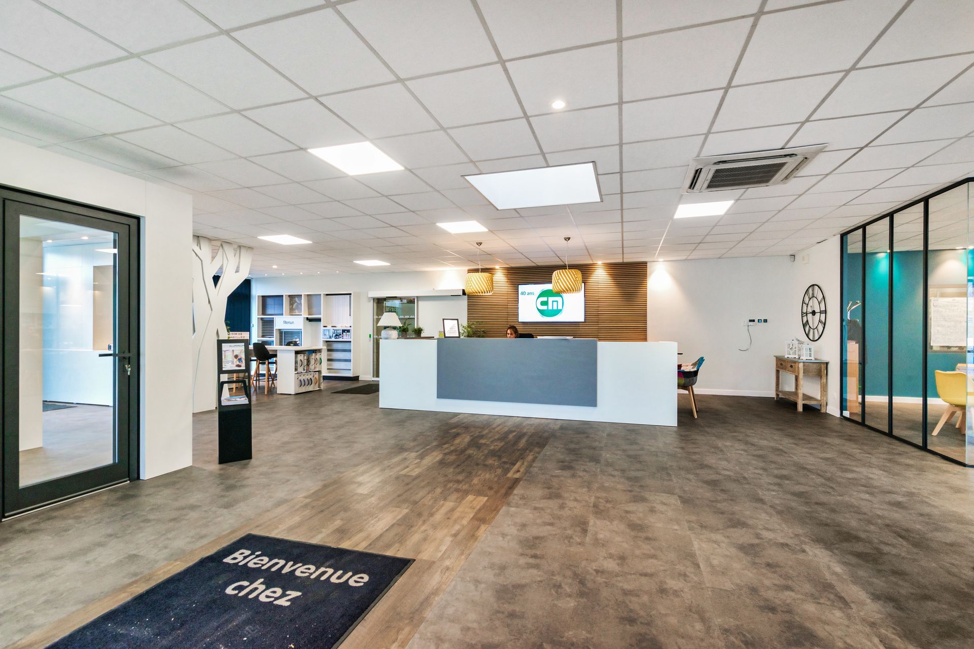 Espace d'accueil avec bureau, logo et paillasson « Bienvenue ». Tons neutres, ambiance chaleureuse.