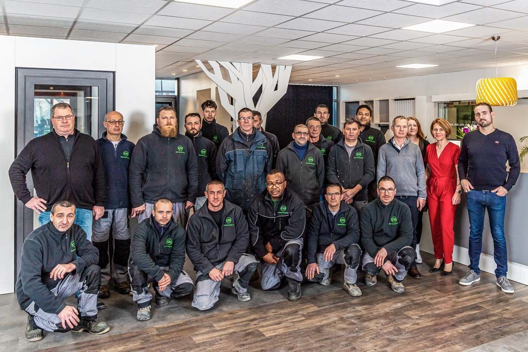 Groupe de personnes posant dans un bureau, la plupart vêtues de chemises noires. Certaines sont agenouillées. Décor moderne.