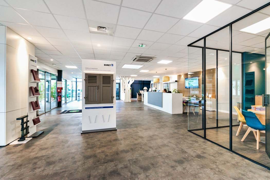 Intérieur de bureaux spacieux avec sols gris, salles de réunion aux parois vitrées et présentoirs mettant en valeur les produits.