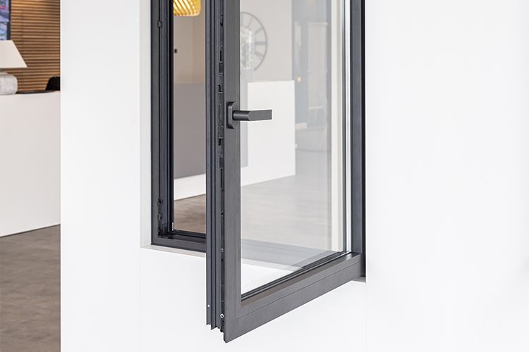 Une fenêtre à battants gris foncé est ouverte contre un mur blanc ; l'intérieur est visible à travers la vitre.