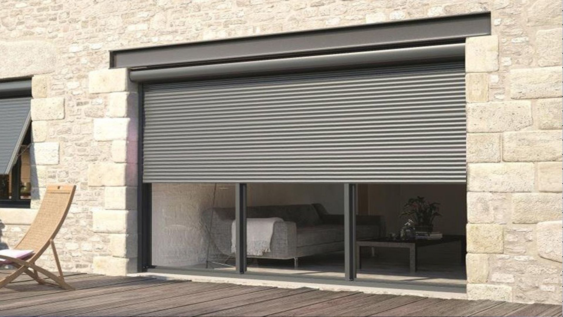 Un volet roulant gris recouvre partiellement une porte vitrée, encastrée dans un mur en pierre.