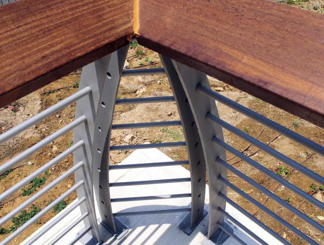 Coin d'une balustrade avec un dessus en bois brun et des barres métalliques grises.