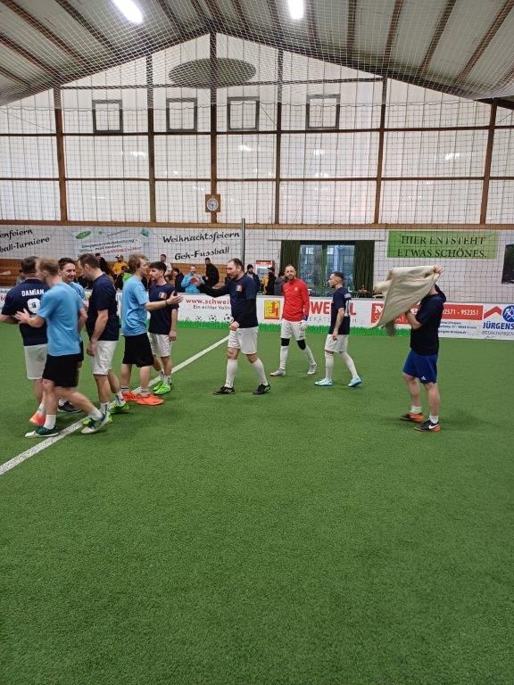 Eine Gruppe von Fußballspielern in einer Halle, einige tragen hellblaue und andere dunkle Kleidung.