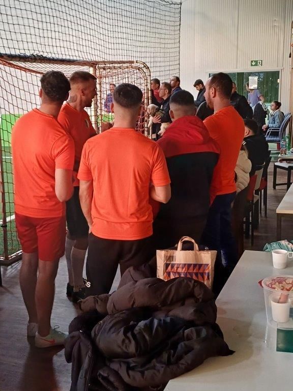 Menschen in orangefarbenen Hemden drängen sich in der Nähe eines Tors und eines Tisches im Innenbereich. Andere Menschen schauen im Hintergrund zu.