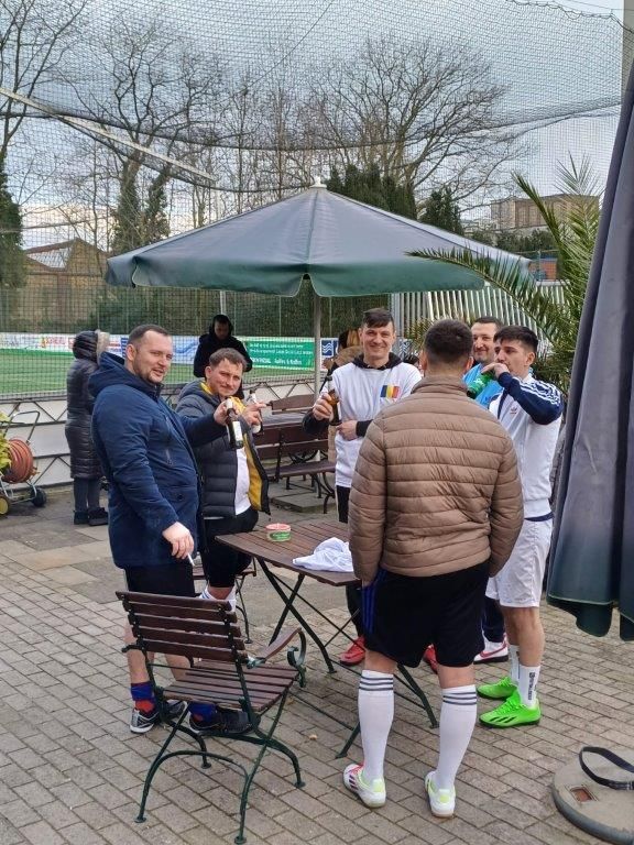 Eine Gruppe von Männern in Sportkleidung trinkt im Freien unter einem Sonnenschirm.
