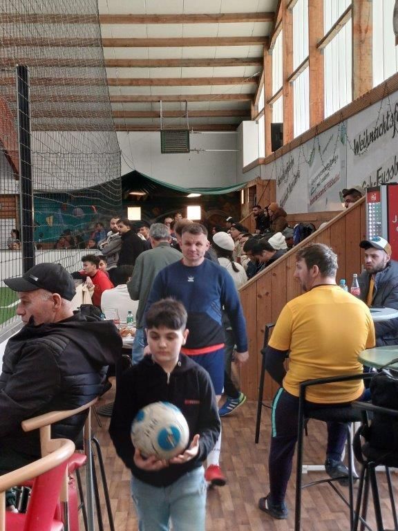 Menschen in einem Fußballstadion; ein Junge hält einen Ball, andere sitzen oder stehen.
