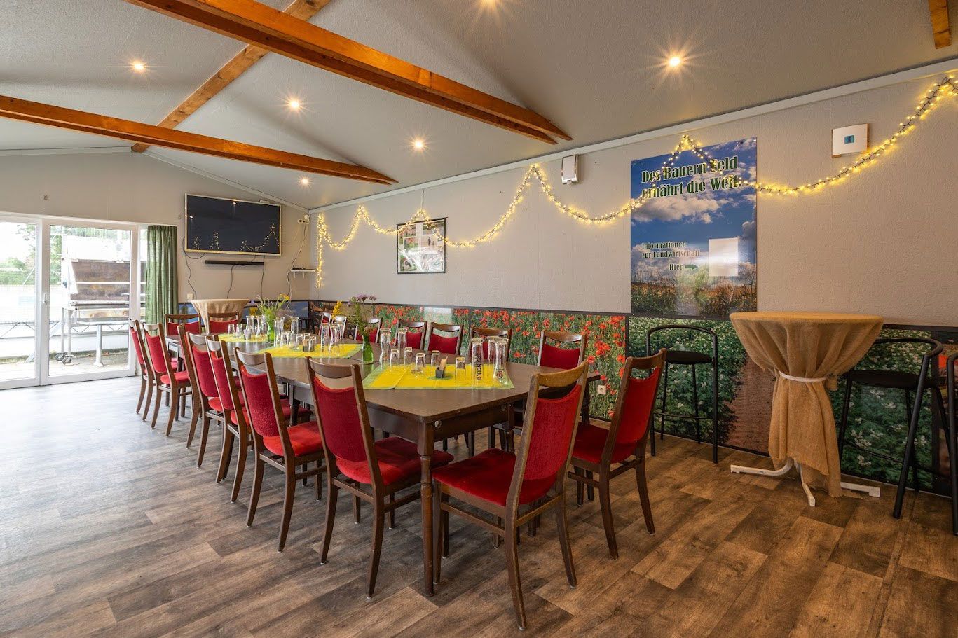 Langer Esstisch, gedeckt für eine Mahlzeit in einem Raum mit roten Stühlen, Holzbalken und einem Poster.